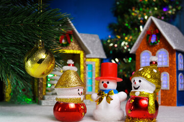 Three snowmen and a ball on a Christmas tree branch against the backdrop of houses