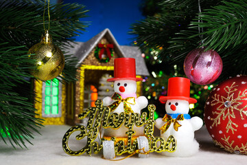 Between two balls on Christmas tree branches are snowmen with letters against the background of a house