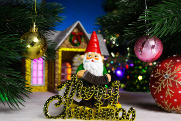 Between two balls on the Christmas tree branches there is a gnome with letters against the background of a house