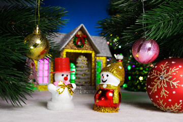 Between two balls on the Christmas tree branches there are two snowmen and a larger ball against the background of a house