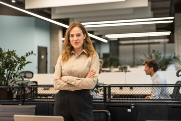 Attractive young businesswoman standing on the table, looking at camera with colleagues on the background