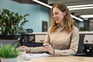 Young business woman is using laptop while sitting in the office, smiling