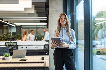Young elegant business woman standing with digital tablet near office window