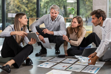 Business people looking at project plan laid out on floor, discussing new project plan in modern office.