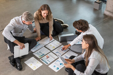 Business people looking at project plan laid out on floor, discussing new project plan in modern office, top view.