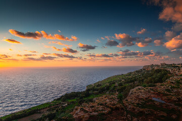 Golden hour sunset at the rugged Dingli Cliffs in Malta, with warm light illuminating the rocky terrain and small clouds over the Mediterranean Sea.