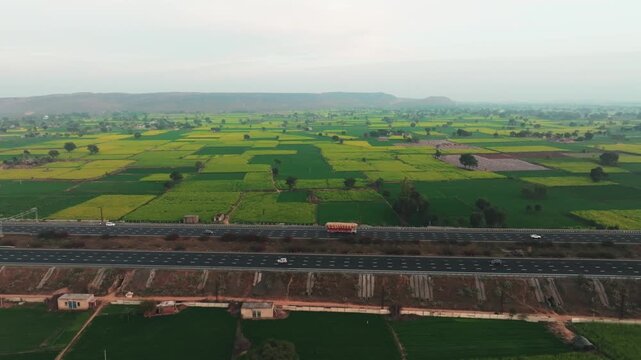 Aerial view of vibrant green and yellow agricultural fields intersected by a grey highway with vehicles, creating a patterned landscape, Alwar, Rajasthan, India.