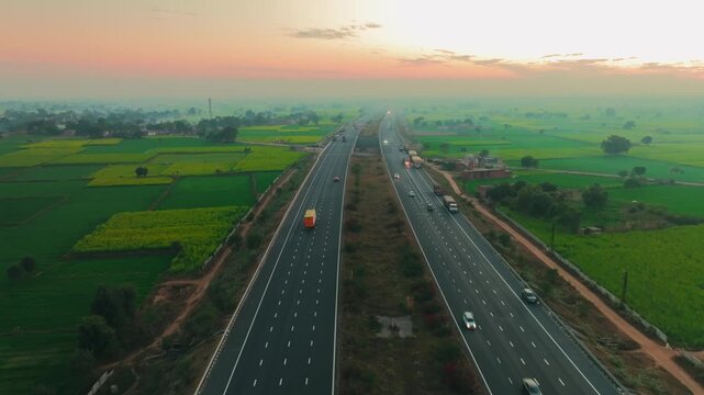 Aerial view of a highway with cars and trucks cutting through a landscape of green and yellow fields under a hazy sky, Alwar, Rajasthan, India.
