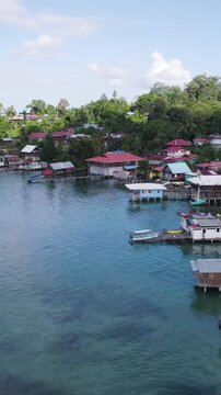 Vertical aerial view of colorful houses lining the shore of Bastimentos Island in Bocas del Toro, Panama on a sunny day.