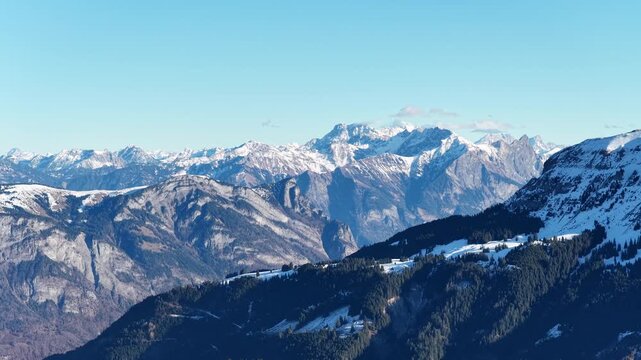 Sweeping aerial view of the Swiss Alps in winter. Showcasing the snowy peaks of Flumserberg and the jagged Churfirsten range overlooking Flums in a majestic sunlit vista.