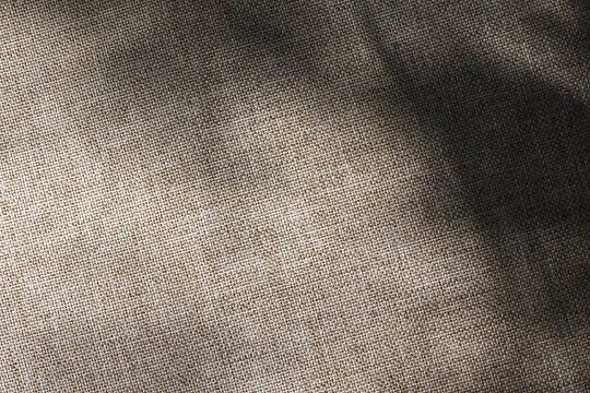 Close up view of woven grey linen fabric texture showing natural fiber detail with dramatic shadow overlay creating somber mood and abstract rustic pattern for background or textile design concept