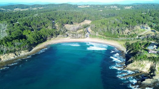 Drone aerial landscape showing seaside waves breaking on sandbar at Mckenzies Beach inlet cove surrounded by bushland forest and suburban homes in Malua Bay South Coast Australia travel tourism nature