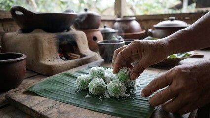 Hands preparing traditional Indonesian Klepon dessert on banana leaf with rustic kitchen background.