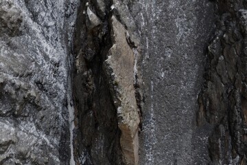 Textured dark rock walls with ice, framing a prominent lighter, angular rock slab. Close-up of rough, natural geology in striking vertical relief
