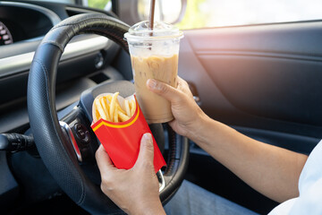 Asian lady holding hamburger and ice coffee to eat in car, dangerous and risk an accident.