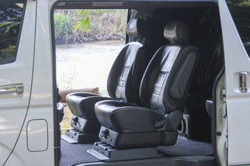 Luxury interior of white passenger van featuring comfortable black leather seat with reclining function invites relaxing journey through nature with open door revealing peaceful outdoor scenery © CoreRock