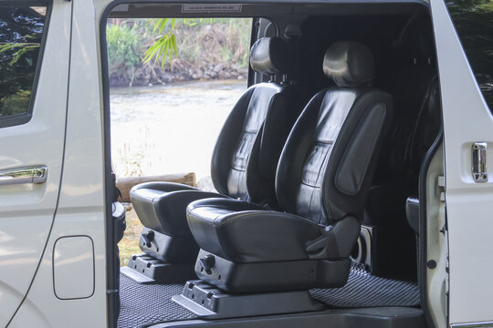 Luxury interior of white passenger van featuring comfortable black leather seat with reclining function invites relaxing journey through nature with open door revealing peaceful outdoor scenery