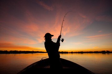 Silueta de pescador con caña en un bote durante un atardecer naranja sobre el río