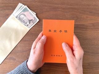 Senior holding pension booklet and cash on wooden table