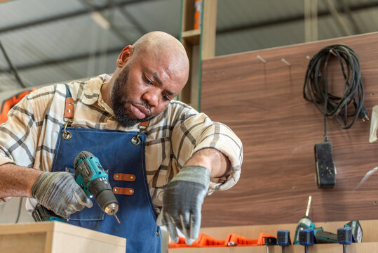 Carpenter man Portrait of Young black skin working in workshop. Happy professional Carpenter holds wooden planks for build furniture in carpentry workshop. carpenter worker make furniture in DIY shop