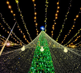 Bright christmas tree lights with glowing bulb in foreground and star on top creating magical festive holiday mood at night