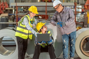 Construction Workers and Supervisor Discussing Project Plans in Factory with Large Metal Rolls and...