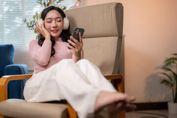 Young woman relaxing on armchair listening to music with wireless headphones and smartphone