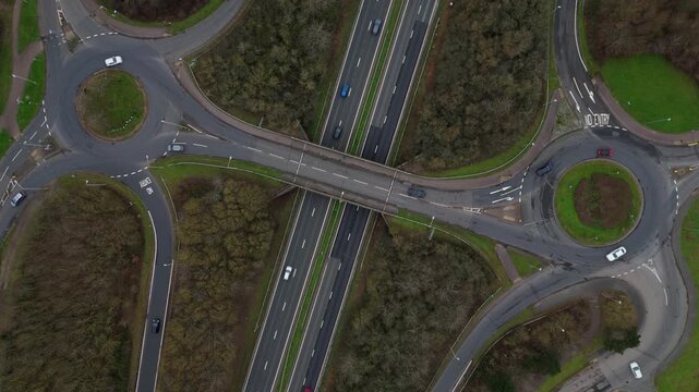 Aerial view of roundabouts interlinked by roads with vehicles cutting through, contrasting with the surrounding green spaces, Leicester, England, United Kingdom.