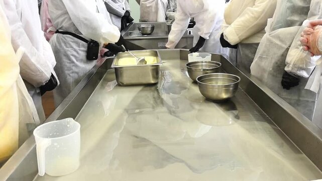 Participants gather around a table to learn cheese-making techniques at a workshop. They use milk and various tools to create different cheese types.
