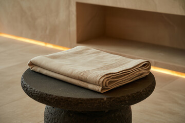 Folded beige towel on a round black stone table with a lighted background in a luxury spa setting