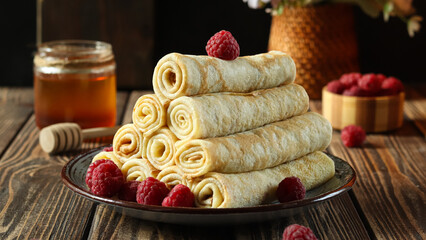 Crepes stacked neatly on a black plate with raspberries and honey in a warm kitchen setting during...