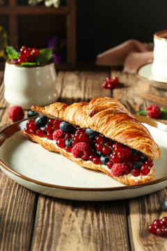 Croissant filled with mixed berries served on a white plate in a rustic setting with wooden table and decorative items