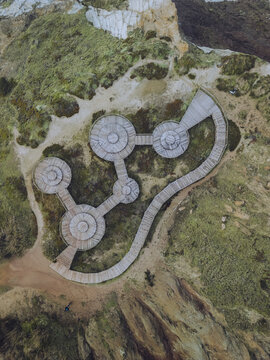 Aerial view of a unique circular wooden structure with connecting pathways amid the coastal landscape, a geometric dance of form and nature, Foz do Arelho, Leiria District, Portugal.