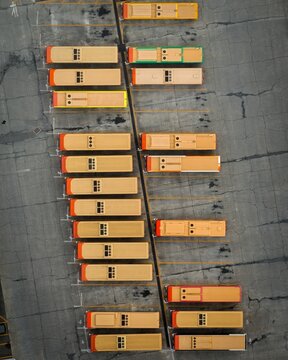 Aerial view of rows of orange and yellow buses sit in neat formation, casting shadows on the concrete ground, Himeji, Hyogo, Japan.