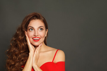 Beautiful surprised woman with curly hairstyle and makeup holding her hand with her face on black background