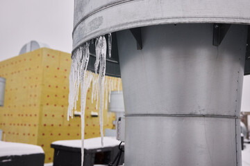Metal vent with hanging icicles, Frozen icicles draping metallic chimney vent, Closeup of icy metal...
