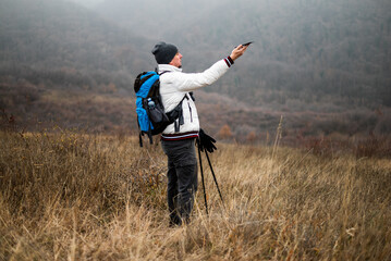 Worried and lost hiker in warm clothing is trying to find signal for his smartphone while hiking in nature. He is appearing confused about the route.