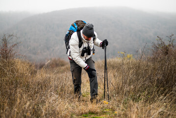 Hiker in warm clothing struggling with knee injury or muscle strain while standing on a forest...