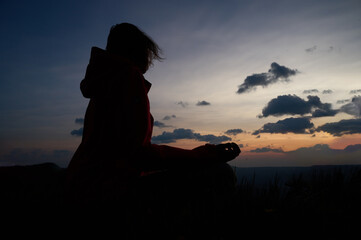 Silhouette of woman meditating at sunrise. Meditation practice seated cross-legged on grass. Golden hour. Peaceful scene of mindfulness and connection with nature.