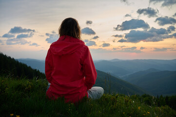 Woman sitting on a yoga mat in the mountains, meditating at sunrise. Peaceful outdoor moment, reconnecting with nature and mindfulness practice in a scenic setting.