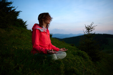 Woman sitting on a yoga mat in the mountains, meditating at sunrise. Peaceful outdoor moment, reconnecting with nature and mindfulness practice in a scenic setting.