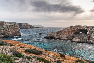 Malta Blue Lagoon landscape. Stunning view of the Blue Lagoon in Comino, Malta, showing the famous turquoise crystal clear waters and the rocky islet of Cominotto under a cloudy sky.