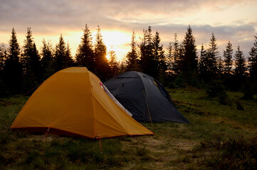 Two tents at sunrise in the morning on the hill. Two tents pitched on a hilltop, bathed in the soft, colorful light of the morning sun. Camping tent on the hill in the morning.