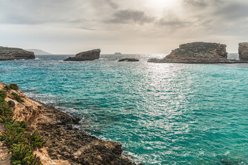 Malta Blue Lagoon landscape. Stunning view of the Blue Lagoon in Comino, Malta, showing the famous turquoise crystal clear waters and the rocky islet of Cominotto under a cloudy sky.
