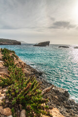 Malta Blue Lagoon landscape. Stunning view of the Blue Lagoon in Comino, Malta, showing the famous turquoise crystal clear waters and the rocky islet of Cominotto under a cloudy sky.