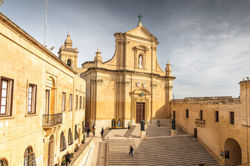 The grand facade of the Cathedral of the Assumption in the Cittadella of Victoria, Gozo, featuring wide stone steps and baroque limestone architecture. Travel to Malta.