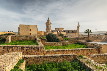 Gozo citadella. Scenic view of the ancient stone fortifications and rooftops within the Cittadella of Victoria, Gozo, showing green grass and traditional limestone architecture.
