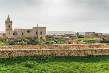 Gozo citadella. Scenic view of the ancient stone fortifications and rooftops within the Cittadella of Victoria, Gozo, showing green grass and traditional limestone architecture.