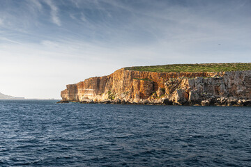 Rugged limestone cliffs of Comino Island in Malta overlooking the deep blue waters of the Mediterranean Sea under a clear afternoon sky. Travel to Malta.