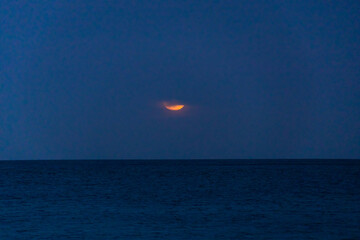 Large glowing full moon rising over the dark horizon of the Mediterranean Sea in Malta, partially covered by soft horizontal clouds during twilight.